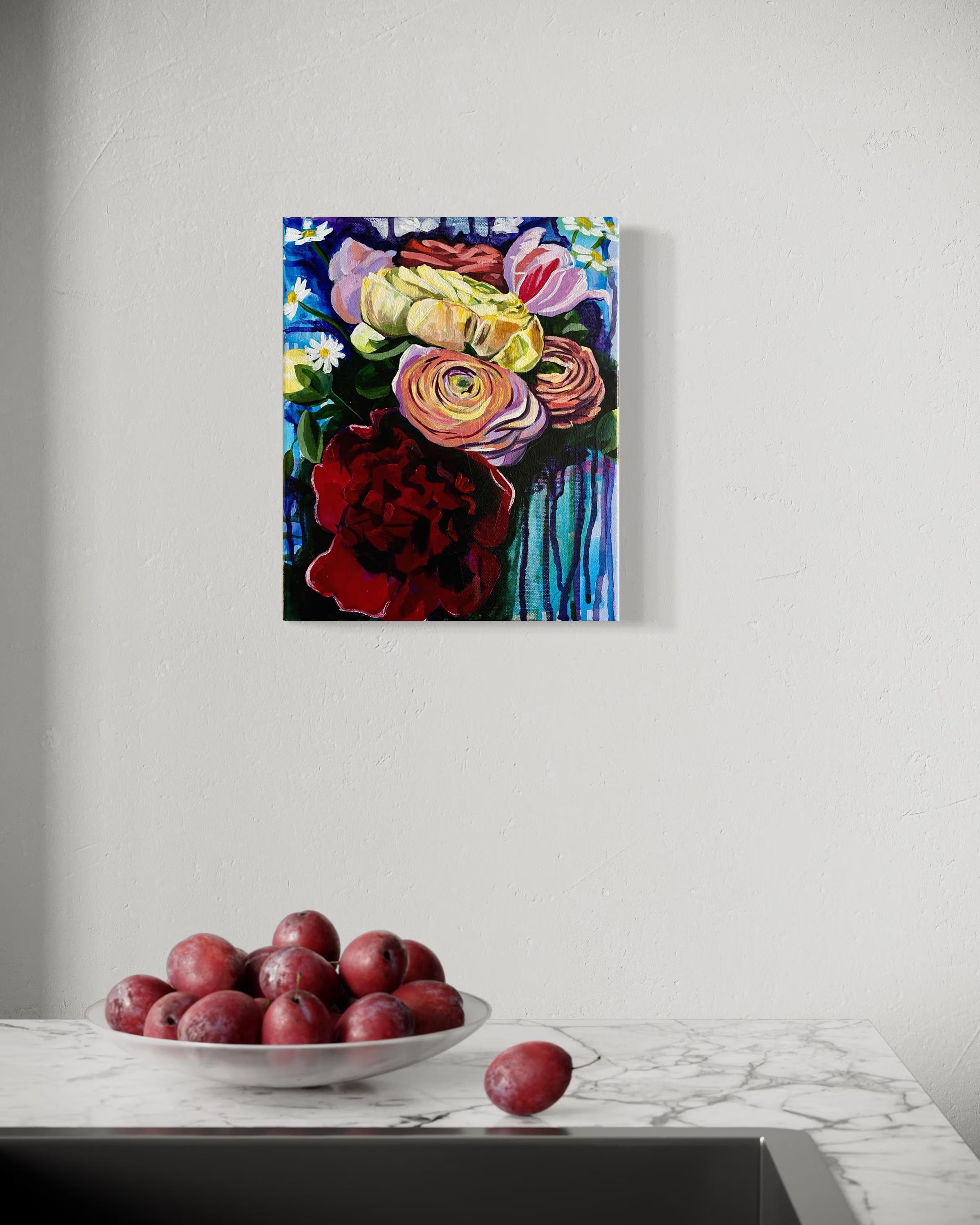 Colorful floral painting on a white wall above a marble surface with plums.